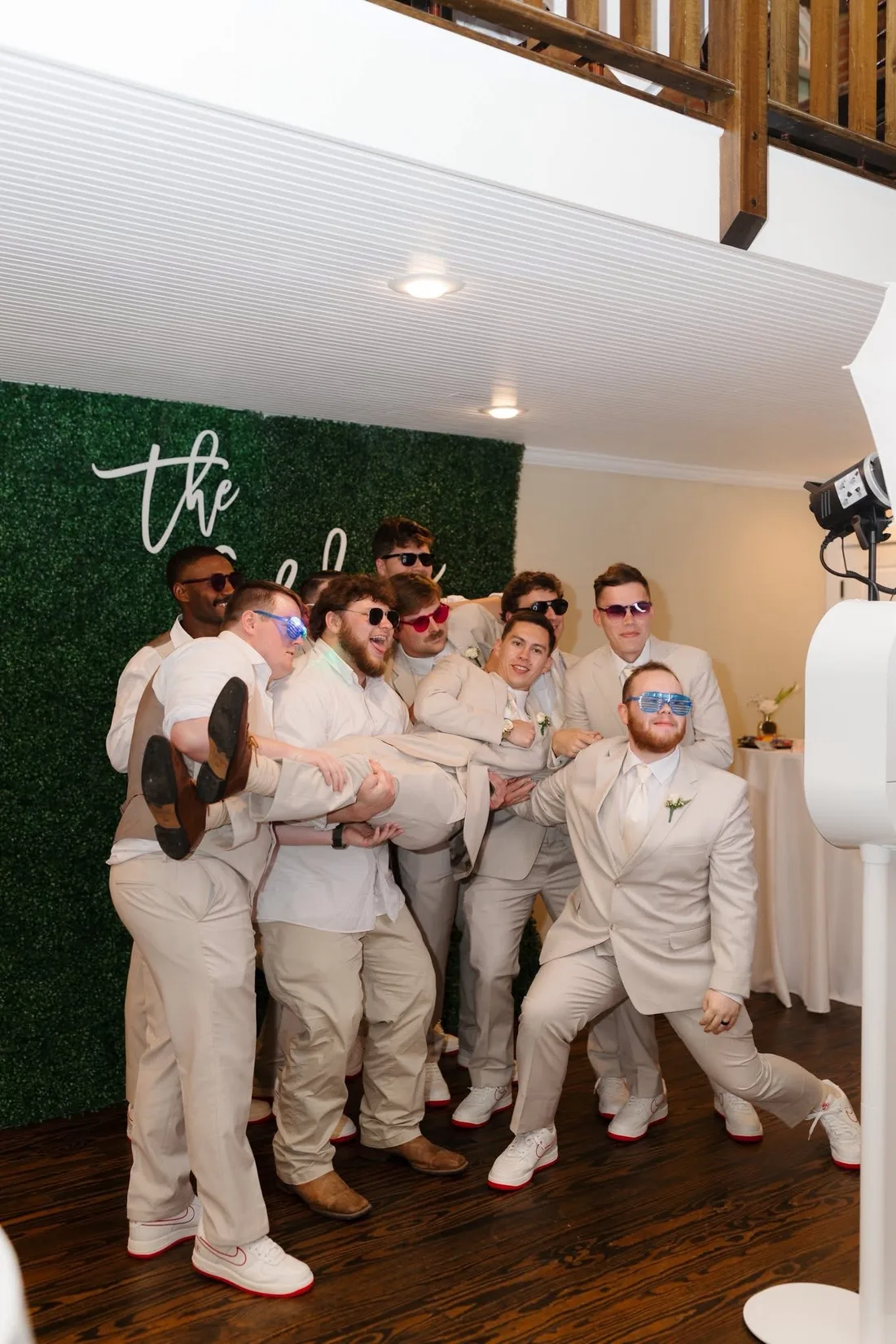 Groomsmen posing together in front of a green hedge wall.