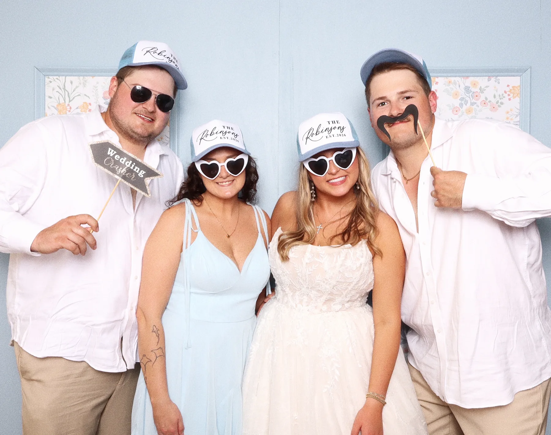 Four guests in custom event caps posing with props in the booth.