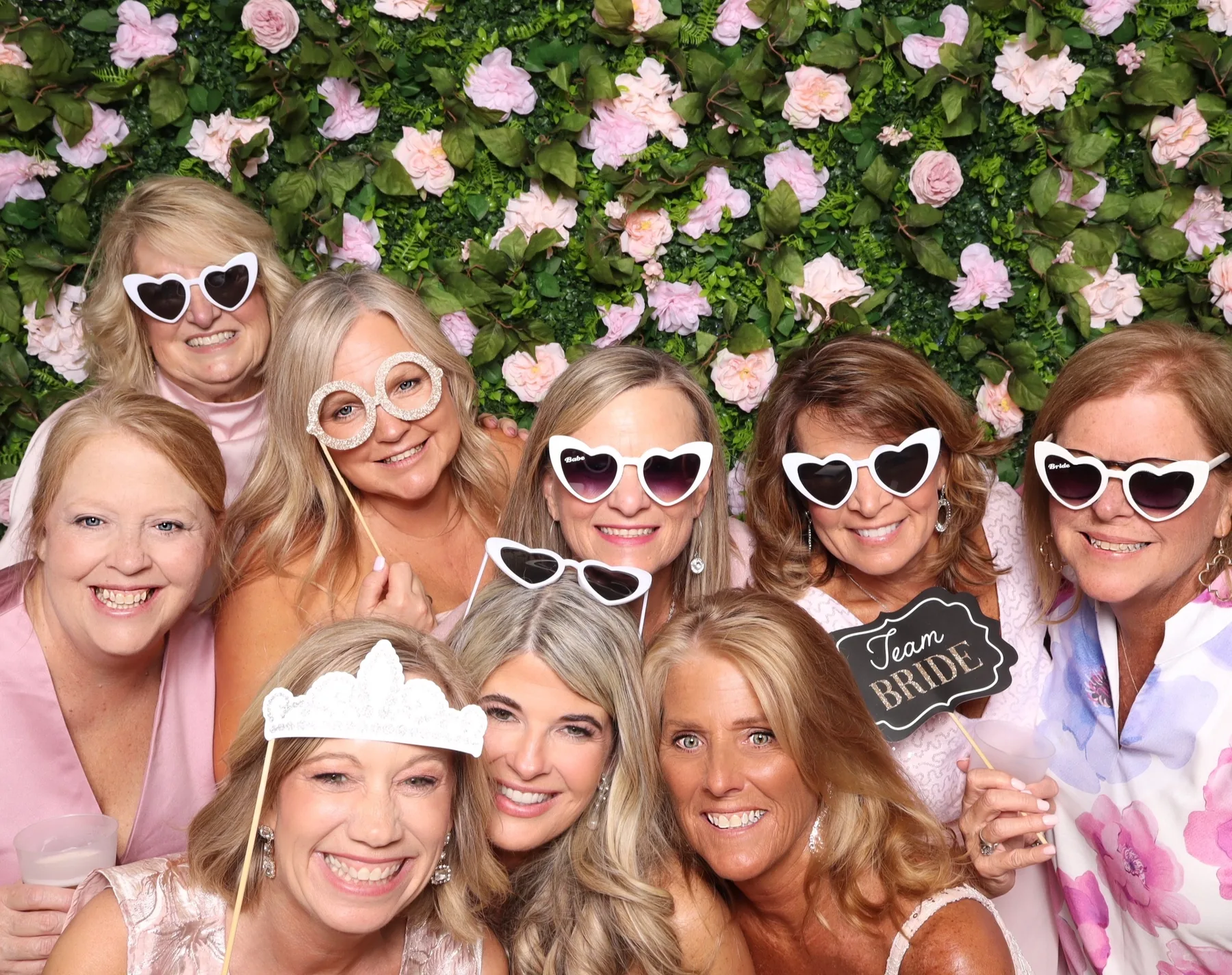Guests posing together with props in front of a pink flower wall backdrop.