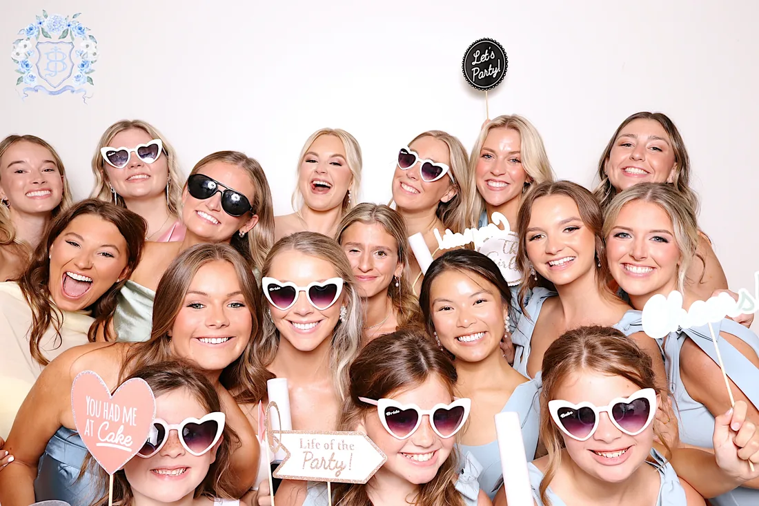 A crowd of guests in heart sunglasses holding party props in the booth.