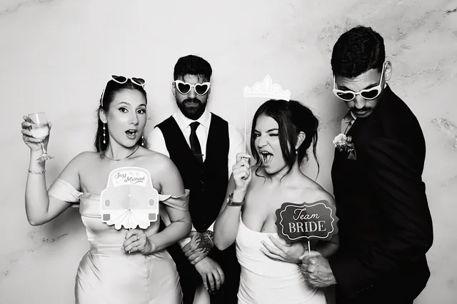 Two couples posing with props in a black and white booth photo.