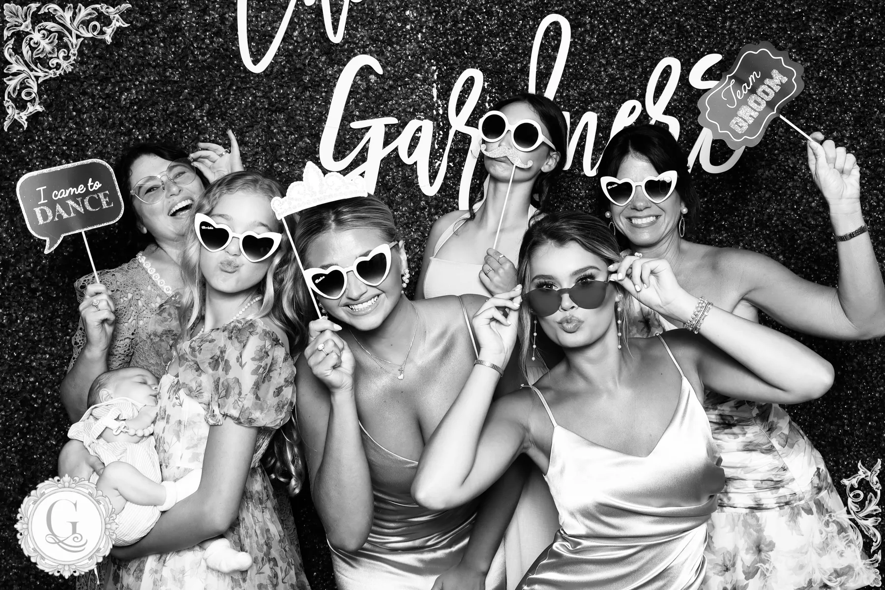 Wedding guests posing with heart sunglasses and props, framed by the couple's custom photo overlay.
